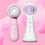 Two Clarisonic facial cleansing devices are artfully displayed against a pink backdrop. The left device boasts a pink hue with a circular brush head, while the right is elegantly white and lavender with intuitive button controls. Both models feature Daily Cleanse and Smart settings for personalized skincare.