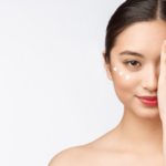 A woman with bare shoulders covers one eye with her hand. She smiles slightly, showcasing skincare dots under her exposed eye. The white background highlights her serene expression and clear, radiant skin, underscoring the effectiveness of her skincare routine.