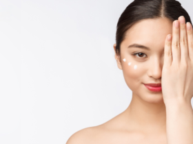 A woman with bare shoulders covers one eye with her hand. She smiles slightly, showcasing skincare dots under her exposed eye. The white background highlights her serene expression and clear, radiant skin, underscoring the effectiveness of her skincare routine.