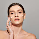A beautiful woman applying white cream on her face, showcasing the latest beauty trends in skincare.