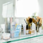 A neatly arranged collection of Makeup And Beauty Products, including skincare bottles, brushes, and an electric toothbrush, all placed on a glass shelf