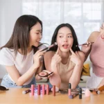 Three women applying makeup in front of a mirror, showcasing how TikTok impacted beauty trends and routines.