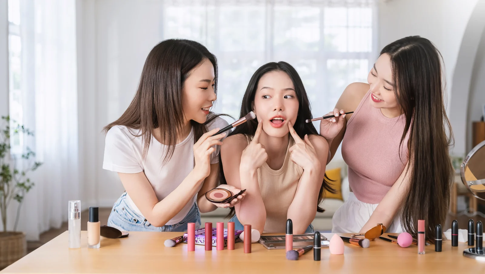 Three women applying makeup in front of a mirror, showcasing how TikTok impacted beauty trends and routines.