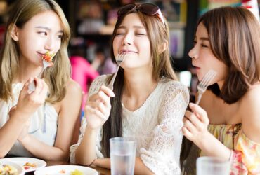 Three friends enjoying food together at a restaurant, sharing laughs and savoring delicious meals.
