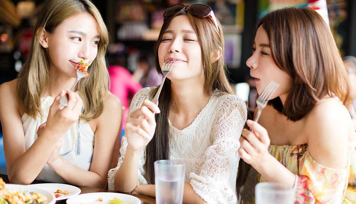Three friends enjoying food together at a restaurant, sharing laughs and savoring delicious meals.